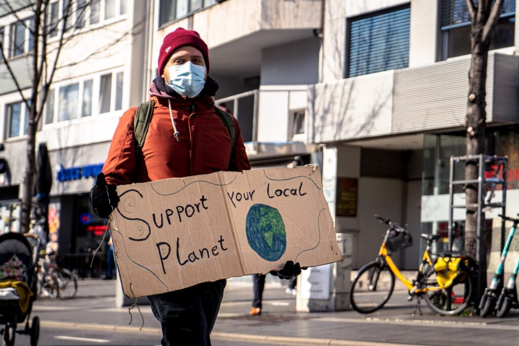 a man holding a peace of carboard box that show a sentence : Support Your Local Planet